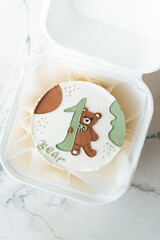 Little birthday bento cake in a gift box decorated with cute cream teddy bear holding digit one. Birthday cake for a one year old child on the white marble background. Flat lay