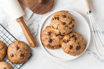 Fresh chocolate American chip cookies with nuts and chocolate drops on white marble background. Flat lay of cookies with stylish cutlery and pastry chef accessories. Recipe of homemade cookies concept