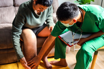 Male Medical Professional in Scrubs and Face Mask Examining Patient's Leg at Home