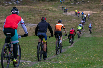 Group cyclists riding uphill trail behind each other at mountain bike race