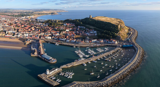 Aerial view of Scarborough Harbour in the morning light, with yachts docked in the marina, the town’s colourful houses, and Scarborough Castle standing on the headland above the North Sea.