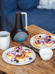 Cheese pancakes with sour cream and jam served with tea on a wooden table.