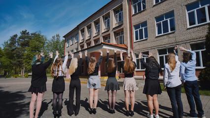 Group of happy students waving goodbye to their school on the last day, celebrating graduation and...
