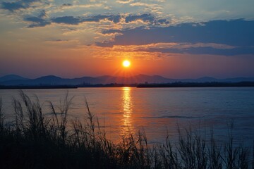 Obraz premium A serene river landscape at sunrise, showcasing vibrant colors reflected on the water's surface and silhouetted grass along the shore.