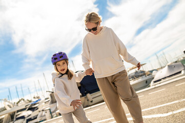 Woman in sunglasses guides little girl on rollerblades