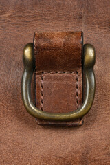 A detailed close-up shot of an antique brass-colored metal D-ring attachment on a piece of rustic brown leather
