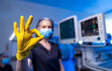 Doctor sends good news. A healthcare worker in a mask and gloves signals approval in a clinical...