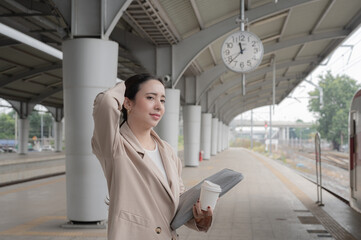 Fototapeta premium A smiling young office worker is standing on a train platform, waiting for a sky train.