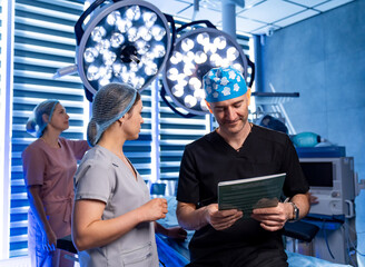 Surgeons prepare for a complex operation. Two doctors discuss patient info in an operating room with modern surgical lights and tools.