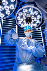 Surgeon gets ready in OR. A surgeon in scrubs displays a surgical tool, ready for an operation in a...
