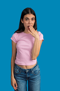 Shocked young woman covering her mouth with hand on blue background