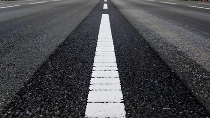 Perspective view of a white dashed line on a dark asphalt road leading into the distance on a clear day