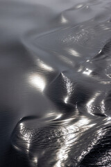 Abstract close-up of cold arctic water with smooth ripples and metallic tones. Sunlight and sky reflections create a molten metal effect on the clean, reflective surface.