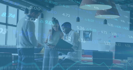 Discussing market numbers, three coworkers reviewing line graphs at table with laptop binder tablet