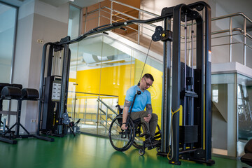 Motivated tired disabled man training upper body muscles with sports training machine for paralyzed...