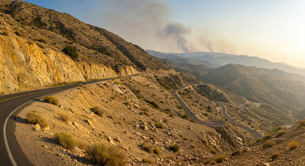 Cliffside road in drought season with wild fire at distance