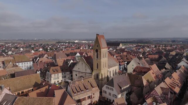 Aerial view of the rustic red rooftops contrasting with the towering Saint-Pierre-et-Saint-Paul Church in the heart of the city, Eguisheim, Grand Est, France.