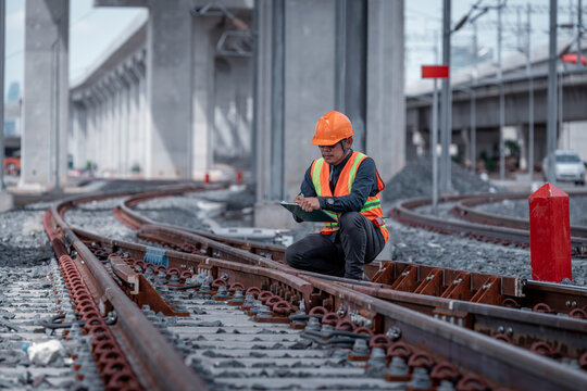 Construction engineer inspecting railway track industrial documents in hand while examining rail structure closely construction, safety and professional project management transportation development.