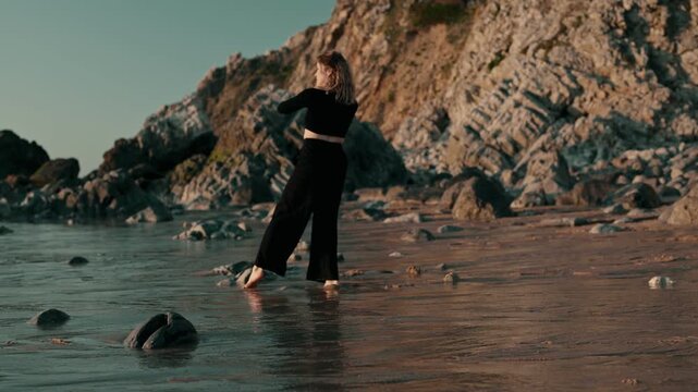 An artistic dancer gracefully moves on a rocky seaside during sunset, capturing the harmony between human expression and natural beauty.