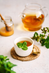 Pfefferminztee in einer Tasse und einer Glaskanne und Honig in einem Einmachglas auf einem weißen Tisch. Kräutermedizin, Teepause.