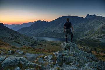 Fototapeta premium Man Standing on Rocks Overlooking Mountain Lake