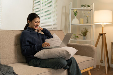 Fototapeta premium Young Asian woman enjoying a peaceful moment reading a book near window. Calm lifestyle, self-learning, and mindfulness at home.