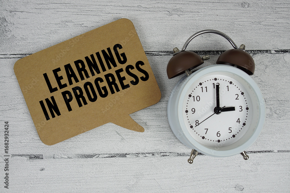 Poster learning in progress text with alarm clock on wooden background
