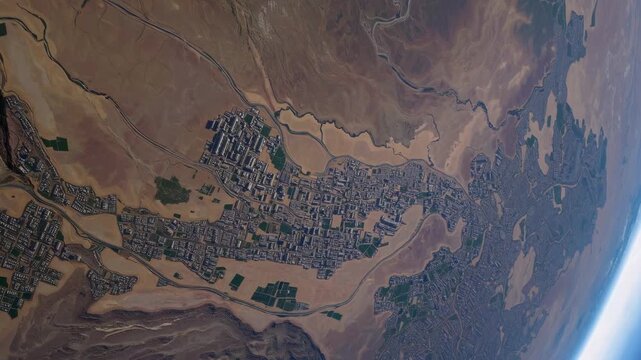 The city is surrounded by desert landscapes, with the city structures creating a striking contrast. Green fields are scattered near the city, blending with the desert terrain.