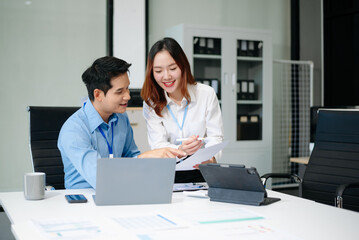 Obraz premium Two young Asian professionals engaged in teamwork and business discussions in modern office embodying corporate