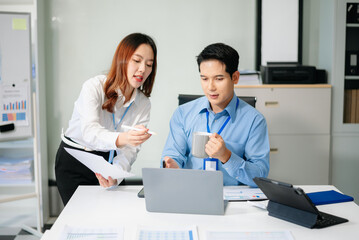 Fototapeta premium Two young Asian professionals engaged in teamwork and business discussions in modern office embodying corporate