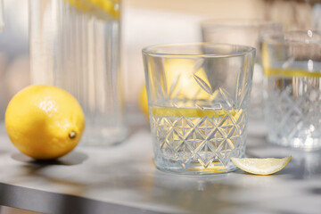 Close-up of a patterned glass filled with lemon water and slice, placed on a sunlit table with a...