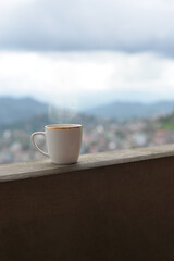 A steaming cup of tea rests on a concrete balcony, with blurred hills fading softly in the background