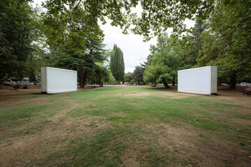 Fototapeta premium Two large white rectangles stand in a green field with various trees, suggesting an outdoor art installation or display area.