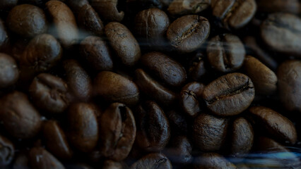 Close-up pile of roasted coffee beans. The rich, deep brown tones of the beans are prominent, with some areas appearing darker