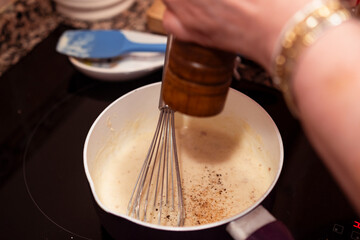 Grinding pepper over bechamel sauce on a pan with whisk. Cooking bechamel sauce for italian lasagna.