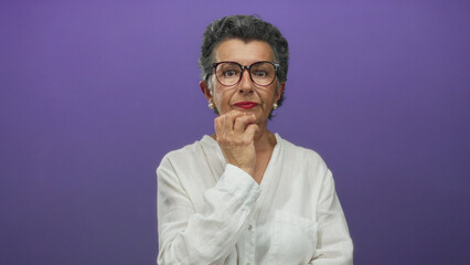Obraz premium Woman with grey hair and glasses in white blouse thinking against a vibrant purple background, suggesting contemplation and wisdom in a modern studio setting.