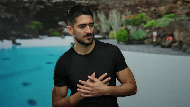 Young man at a resort poolside clutching his chest in discomfort, surrounded by lush outdoor hotel scenery, conveying a sense of pain against a tropical backdrop.