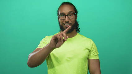 Man pointing finger toward camera in teal studio wearing neon green shirt and glasses; greeting confidence.