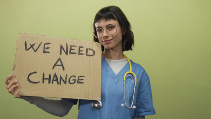 Woman nurse wearing blue scrubs holds cardboard sign reading we need a change in studio; hope activism reform.