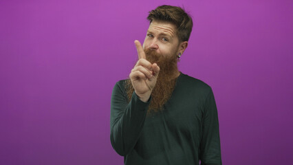 Man with brown beard pointing index finger upright in bright purple studio to signal attention; caution reminder.