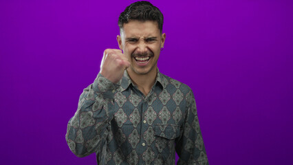 Young man expressing emotion with clenched fist against vibrant purple wall showcasing patterned...