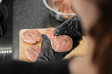 Professional hands wearing black protective gloves skillfully shaping raw meat cutlets on a wooden board for delicious homemade meal preparation