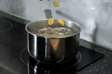 Delicious pasta falling into a shiny stainless steel pot of boiling water on a modern induction hob, symbolizing home meal preparation
