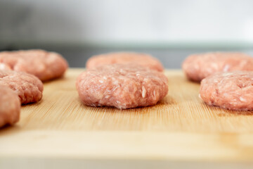 Several uncooked raw meat cutlets are carefully arranged on a light wooden cutting board, emphasizing healthy, fresh home cooking and thoughtful meal preparation