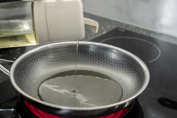 Cooking oil is poured into a hot frying pan on a modern induction hob, symbolizing healthy meal...