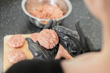 Hands in black gloves meticulously shaping a raw meat cutlet from ground beef for a delicious...