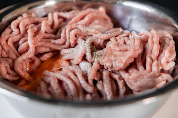 Raw ground pork seasoned with salt and pepper in a metal bowl, with an egg yolk, prepared for making delicious homemade cutlets