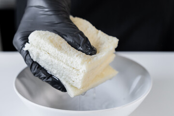 Professional chef in protective black glove firmly squeezing two soaked bread slices over a white...