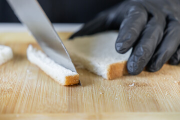 Professional gloved hand precisely slicing fresh white bread with a sharp knife on a wooden board, highlighting meticulous food preparation and culinary hygiene
