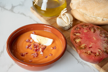 Spanish salmorejo cream decorated with serrano ham and boiled egg, with ingredients around, such as tomato, bread, garlic and olive oil
